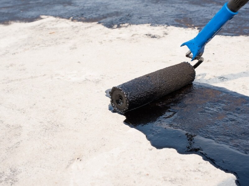 Paint roller used to waterproof a balcony with a black liquid membrane.