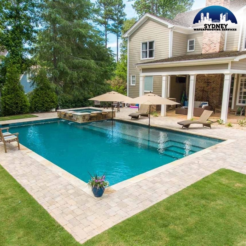 Serene backyard showcasing Pool & Pond Waterproofing in Sydney with a crystal-clear pool, spa, lounge chairs, umbrellas, and lush garden surrounds.